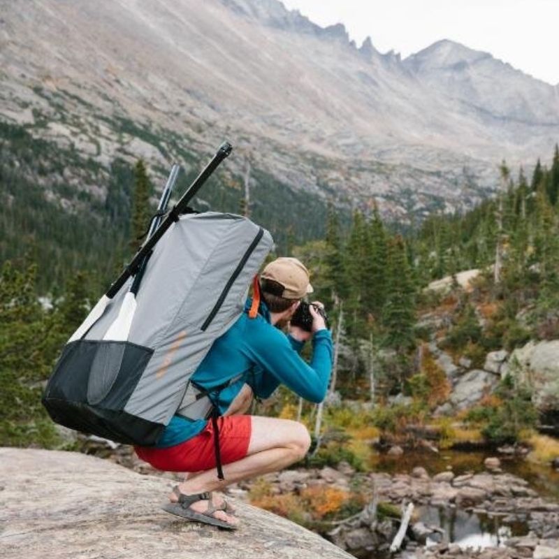 Hiker using Oru Kayak Pack backpack while taking photos in mountain scenery