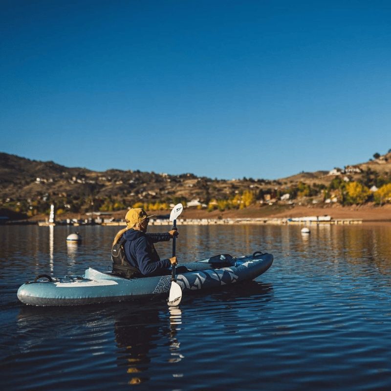 Solo kayaker paddling Kokopelli Platte kayak in smoke blue along a river with rock formations