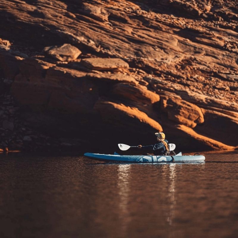 Person kayaking on a lake with the Kokopelli Platte kayak in smoke blue during calm weather