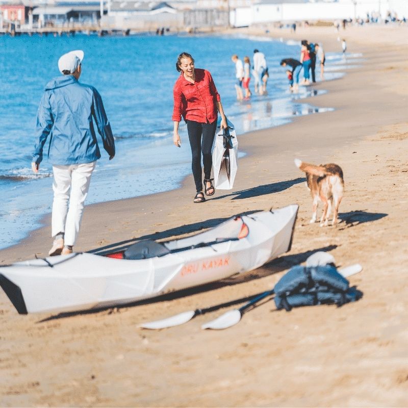 Oru Kayak Inlet on a beach, people preparing to paddle with a dog nearby